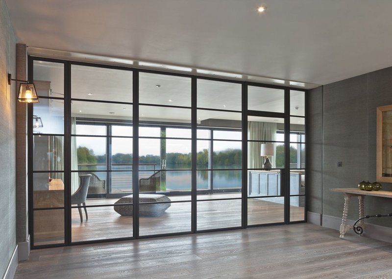 Architectural Bronze Casements' large bronze screen with single Slimline door in a lakeside new-build. Light flows, bringing the view into the hall. Hamilford Design architects.