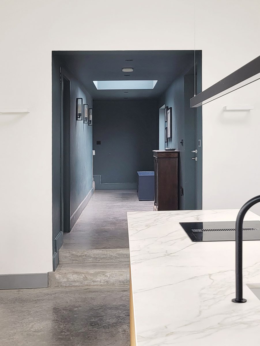 The top-lit dark-painted corridor gives a sense of compression before the big gesture of the living room.